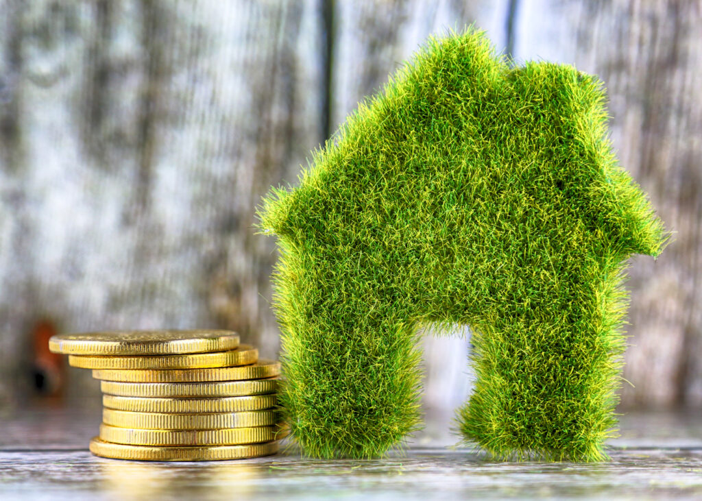 Eco-friendly house model made of grass with coin stacks, symbolising sustainable energy investments.
