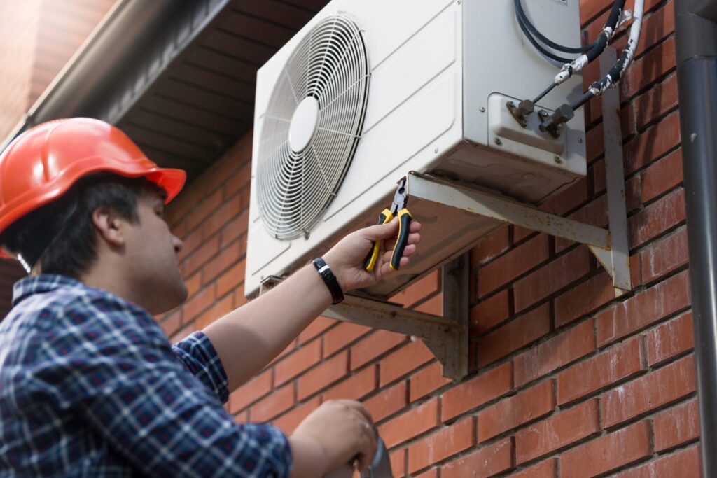 Technician installing an air source heat pump on a brick wall.